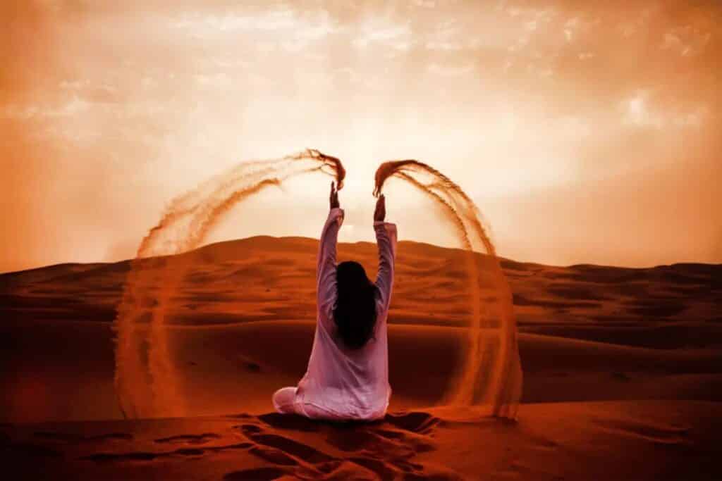 jeune femme assise dans le désert du Sahara au Maroc et jetant du sable fin